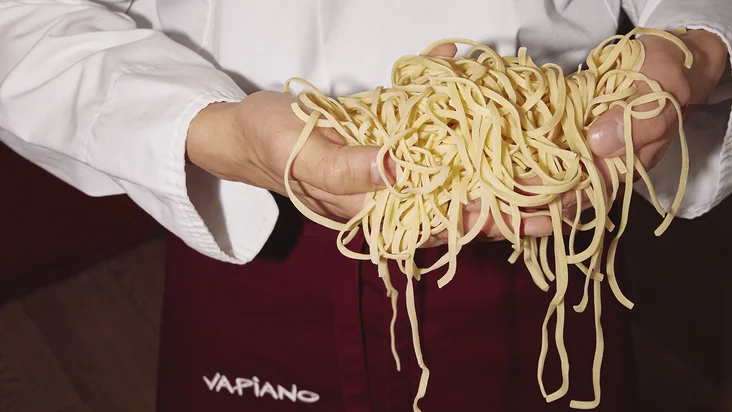 Vapianisti hält hausgemachte Linguine in den Händen.