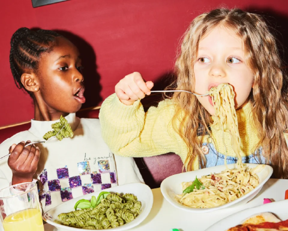 Zwei Kinder sitzen im Restaurant und essen Pasta. 