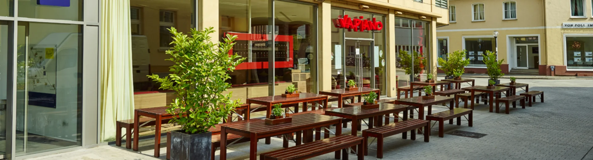 Außenansicht vom VAPIANO Osnabrück mit Bänken, Tischen und Pflanzen im Außenbereich. 