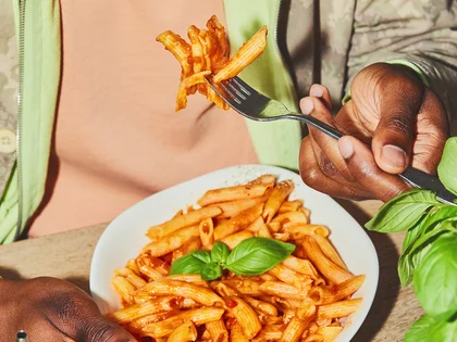 Eine Person sitzt am Tisch und isst Pasta mit Besteck. 