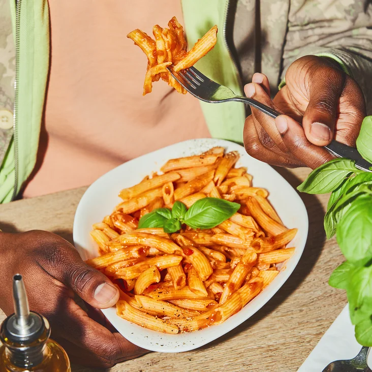 Eine Person sitzt am Tisch und isst Pasta mit Besteck. 