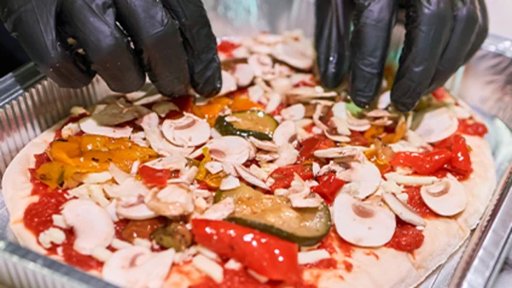 Eine Pinsa wird mit Gummihandschuhen belegt.