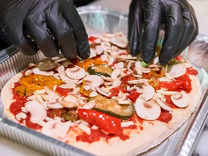 Eine Pinsa wird mit Gummihandschuhen belegt.