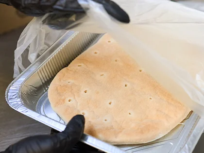 Der Pinsa-Teigling wird mit Handschuhen aus der Verpackung geholt. 