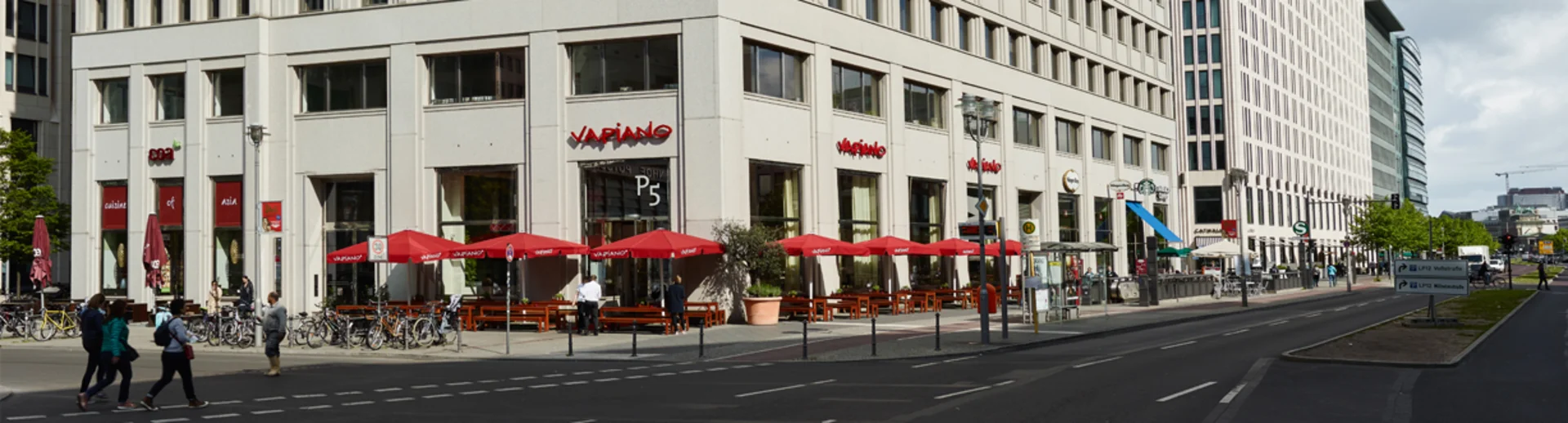 Ein hohes Gebäude an einer Hauptstraße mit dem VAPIANO Berlin Potsdamer Platz im Erdgeschoss.