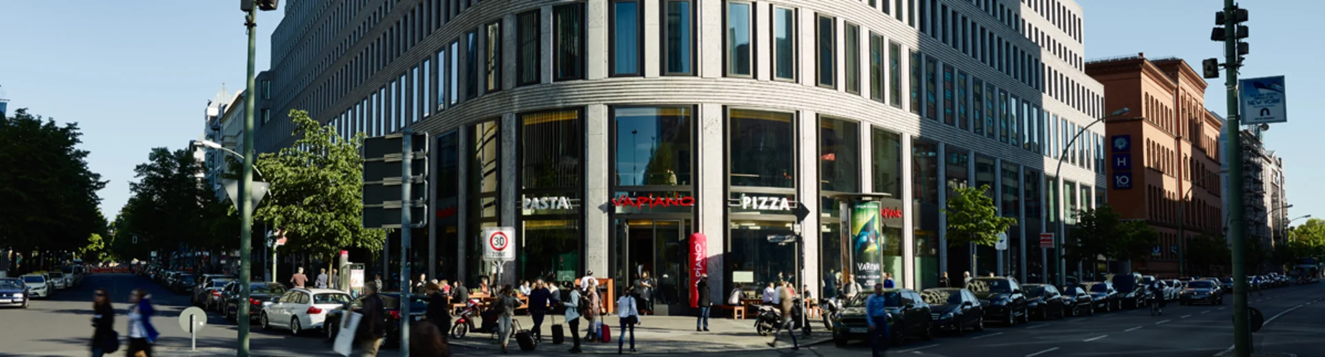 Ein hohes Gebäude an einer Hauptstraße mit einem VAPIANO im Erdgeschoss.