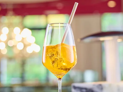 Ein honiggelber Drink mit Zitrone steht auf einer Bar, stilvoll in Szene gesetzt vor einem warm beleuchteten Hintergrund.