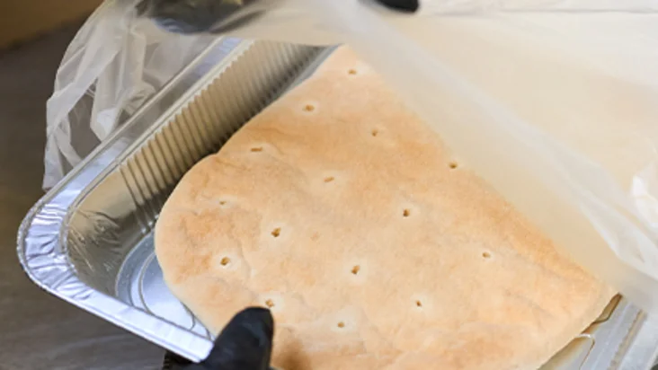 Der Pinsa-Teigling wird mit Handschuhen aus der Verpackung geholt. 