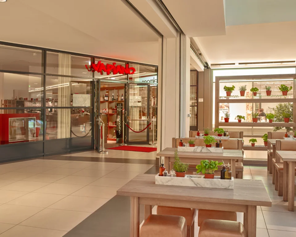 Außenansicht vom VAPIANO Ingolstadt in einer Passage mit Bänken und frischen Kräutern auf den Tischen. 