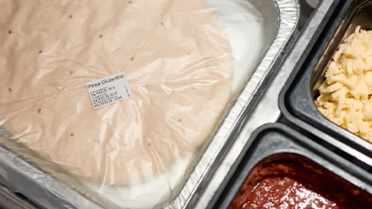 Die Pinsa liegt verpackt in einer Schale neben den Zutaten.