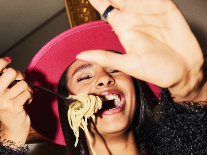Eine fröhliche Frau wird mit Blitz fotografiert und isst Spaghetti. 