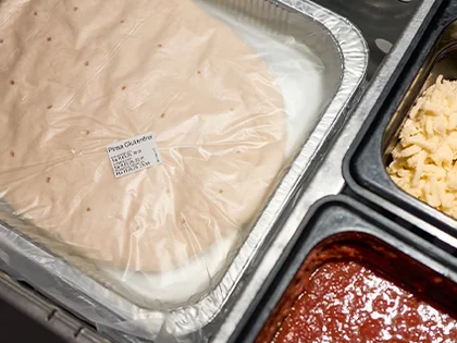 Die Pinsa liegt verpackt in einer Schale neben den Zutaten.