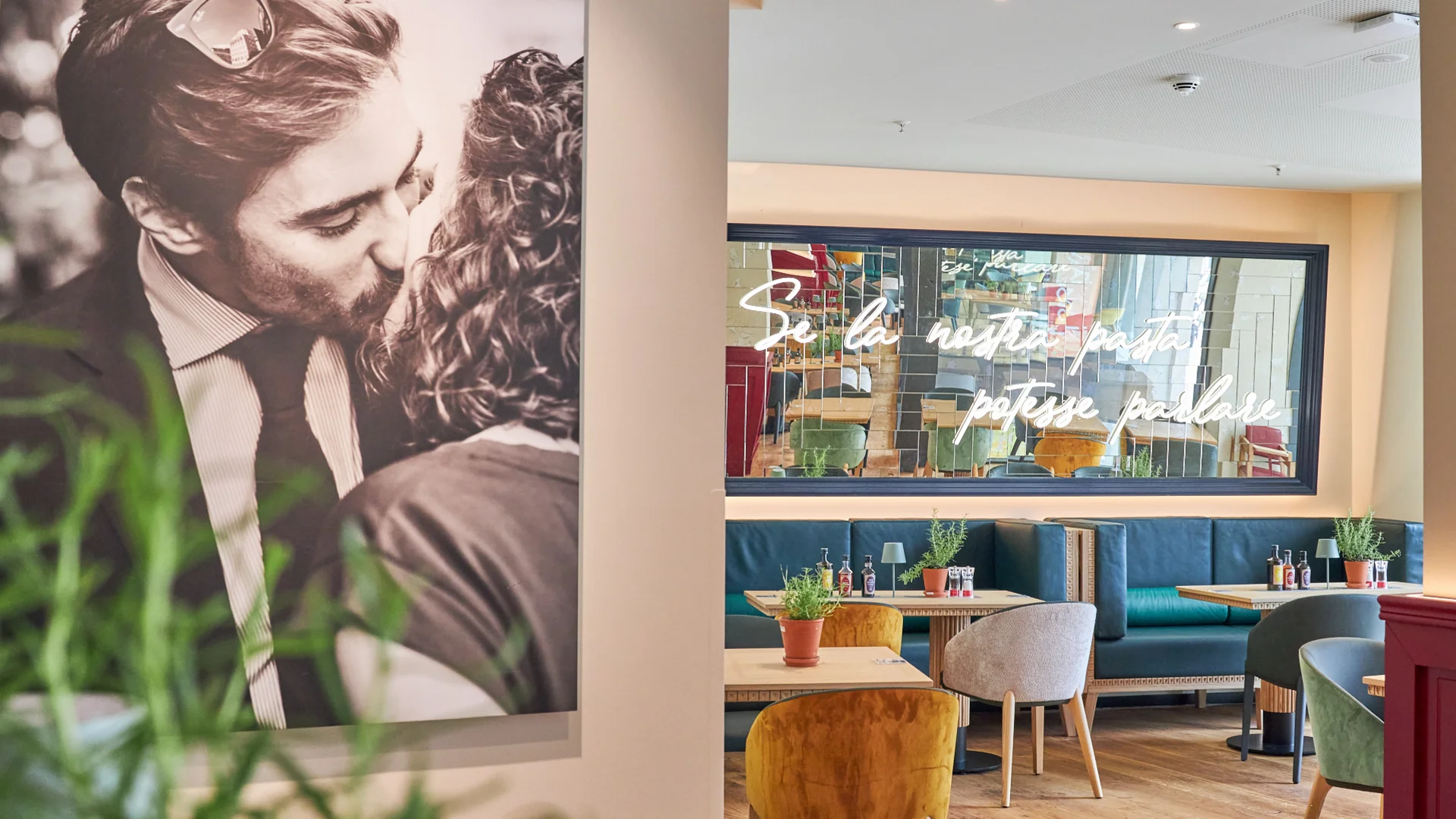 Innenaufnahme vom VAPIANO Hamburg Gänsemarkt mit einem dekorativen Foto an der Wand und einem Spiegel über den Sitzmöglichkeiten im Hintergrund.
