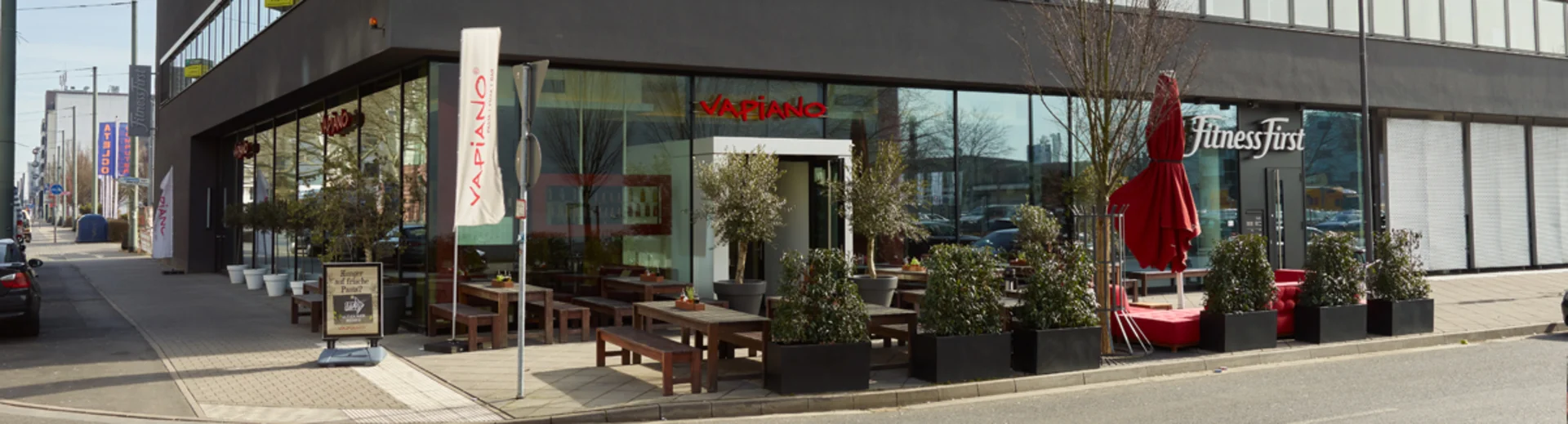 Außenansicht vom VAPIANO Frankfurt im Erdgeschoss mit Bänken und Pflanzen im Außenbereich. 
