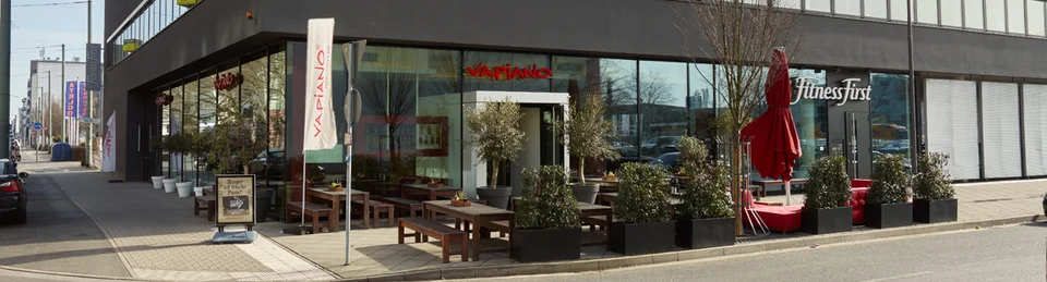 Außenansicht vom VAPIANO Frankfurt im Erdgeschoss mit Bänken und Pflanzen im Außenbereich.