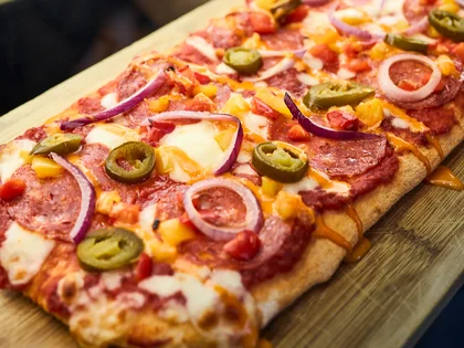 Eine frische Pinsa liegt auf einem Holzbrett. 