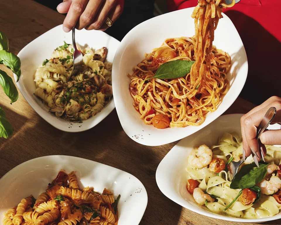 Personen essen verschiedene Pasta-Gerichte am gedeckten Tisch.