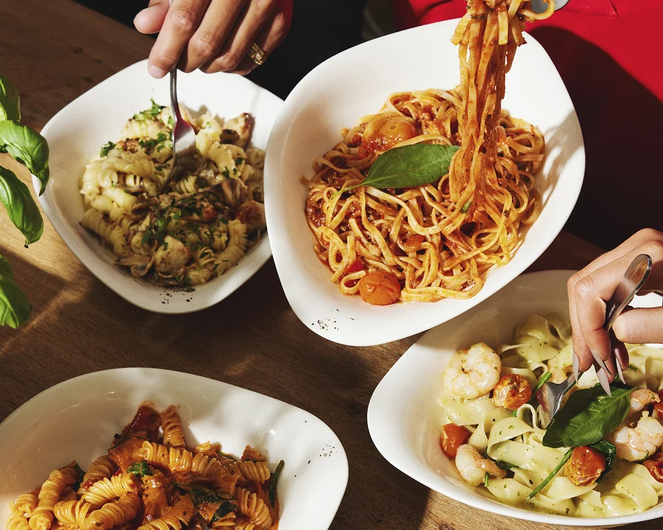 Personen essen verschiedene Pasta-Gerichte am gedeckten Tisch.