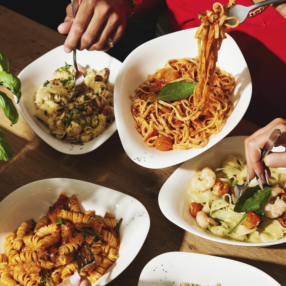 Personen essen verschiedene Pasta-Gerichte am gedeckten Tisch.