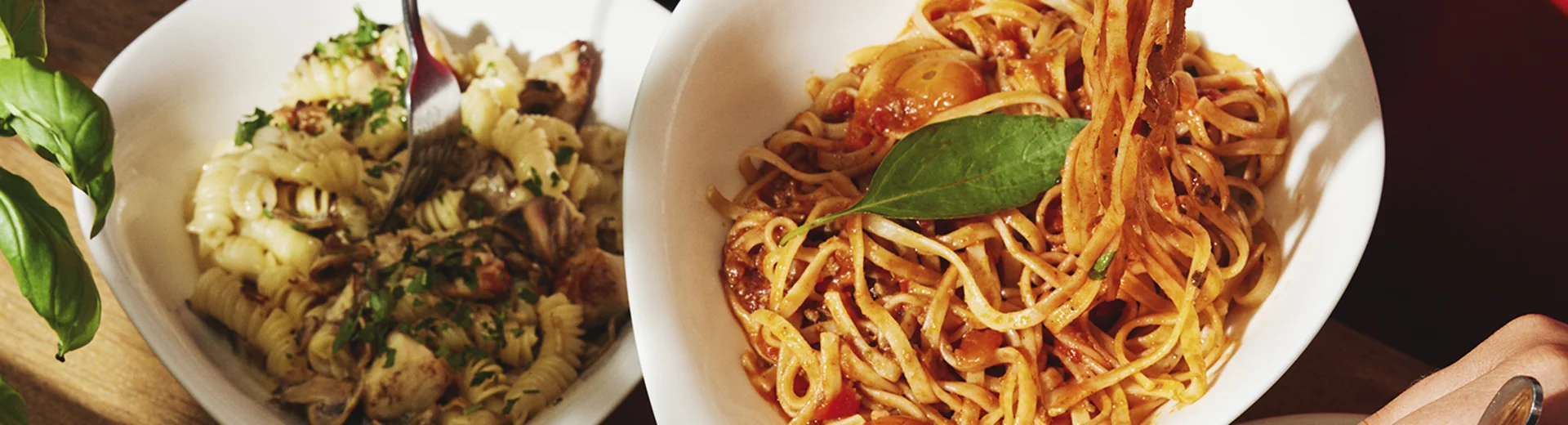 Personen essen verschiedene Pasta-Gerichte am gedeckten Tisch.