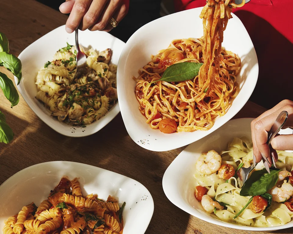 Personen essen verschiedene Pasta-Gerichte am gedeckten Tisch.